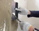 Manos enguantadas aplicando mortero para reparar pared.