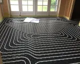 Instalar suelo radiante: tuberías blancas sobre paneles negros, listas para cubrir. Planos en el suelo.