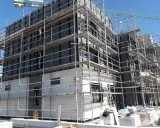 Edificio en construcción con andamios cubriendo la fachada. Se aprecian materiales de aislamiento y paneles, cumpliendo la ley de fachadas.