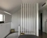 Modern interior with a white slatted divider, suggesting a design to tirar tabique para unir dos habitaciones. Baskets and a window add warmth.