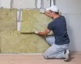 Hombre instalando aislamiento de lana de roca para como aislar una pared.