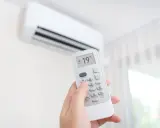 Mano sujetando control remoto de aire acondicionado, ajustando temperatura a 19°C. ¿Es mejor apagar el aire acondicionado o dejarlo encendido?