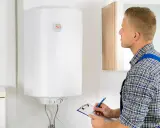 Técnico revisa el funcionamiento termo eléctrico de un calentador de agua, anotando datos en una libreta.