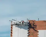 Trabajadores en una plataforma suspendida instalan paneles aislantes en un edificio, parte de un proyecto de sate.
