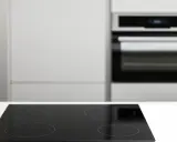 Placa vitrocerámica negra lista para instalar junto a un horno empotrado en una cocina moderna.