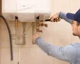 Un técnico ajusta las tuberías de un calentador de agua. Espera que la luz del termo no se apaga para confirmar que todo funciona bien.