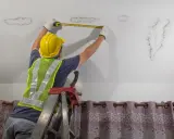 Un trabajador con casco mide manchas de humedad en el techo, evaluando los tipos de grietas y daños.