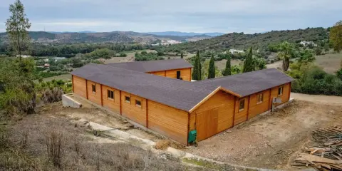 Edificio de madera en forma de L, con tejado oscuro, en un paisaje rural. Ideal para saber cuántos metros cuadrados se pueden construir sin proyecto.