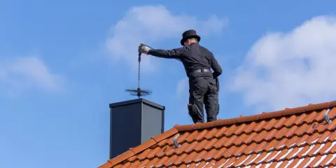 Deshollinador chimenea casero, con sombrero y traje negro, limpia la chimenea desde el tejado.