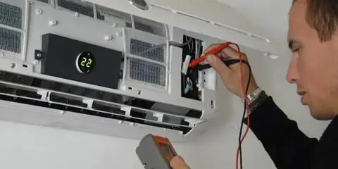 Técnico revisa unidad interior de aire acondicionado con multímetro, cumpliendo la normativa de instalación.