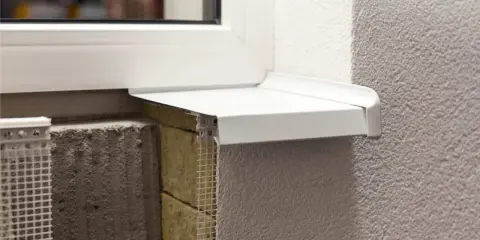 Detalle constructivo de un alféizar blanco sobre aislamiento y mampostería, con malla de refuerzo visible.