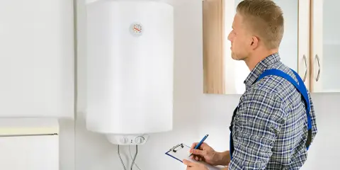 Técnico revisa el funcionamiento termo eléctrico de un calentador de agua, anotando datos en una libreta.