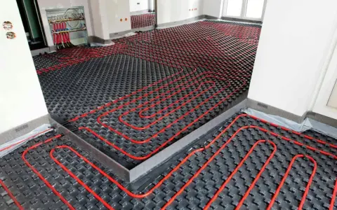 Instalación de un sistema de calefacción por suelo radiante enfria. Tubos rojos serpentean sobre paneles negros en una habitación en construcción.
