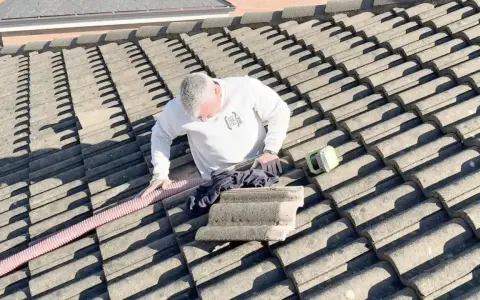 Hombre en tejado trabajando en el aislamiento térmico del tejado. Se ve una manguera rosa y una herramienta verde.