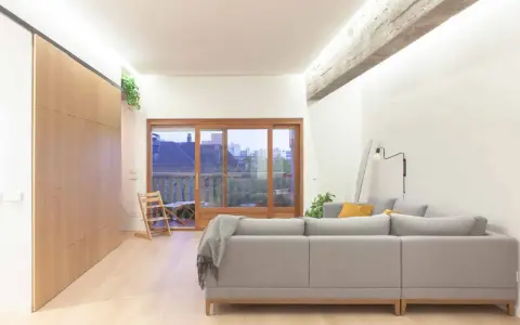 Salón moderno con sofá gris, grandes ventanales y **techos con vigas de hormigón decorar** el espacio con estilo industrial.