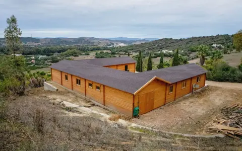 Edificio de madera en forma de L, con tejado oscuro, en un paisaje rural. Ideal para saber cuántos metros cuadrados se pueden construir sin proyecto.