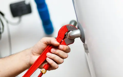 Mano con llave roja ajustando tubería. Es parte de la revisión caldera gas obligatoria para garantizar seguridad y eficiencia.