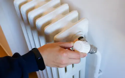 Mano ajustando el termostato de un radiador, parte de los contadores individuales de calefacción central.