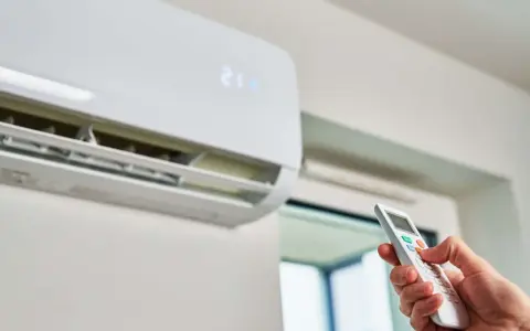 Mano ajustando el control remoto de un aire acondicionado para que gasta menos. La pantalla muestra 21 grados.