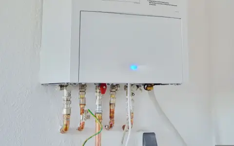 Calentador atmosférico blanco montado en pared con tuberías de cobre y conexiones. Una luz azul parpadea en la unidad, indicando que se puede instalar un calentador atmosférico en el interior.