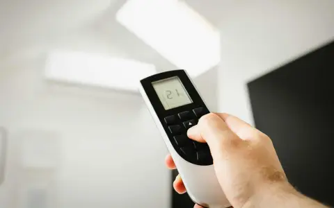 Mano ajustando el mando de aire acondicionado a 21 grados. Instrucciones claras para un confort óptimo.