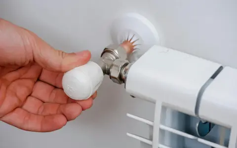 Mano ajustando la perilla de un radiador, mostrando partes de un radiador de agua como la válvula y la conexión.