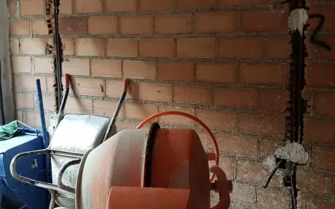 Preparativos para como tirar tabiques de ladrillo: carretilla, hormigonera y pared con ranuras para cables.