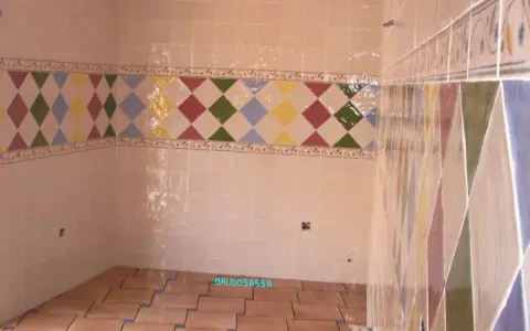 Detalle de azulejos en una pared, mostrando la diferencia entre mortero capa fina y capa gruesa en un diseño de rombos.