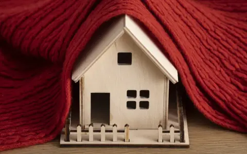 Casa de madera envuelta en manta roja, simbolizando la normativa de aislamiento térmico en viviendas para mantener el calor.