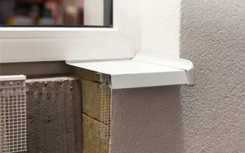 Detalle constructivo de un alféizar blanco sobre aislamiento y mampostería, con malla de refuerzo visible.