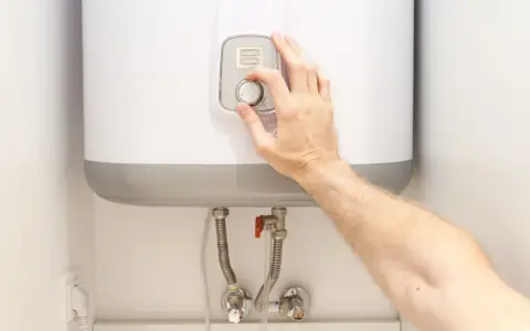 Mano ajustando el termostato de un termo eléctrico. Posiblemente para solucionar problemas de agua caliente.