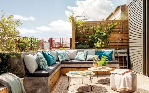 Un rincón perfecto para hacer una terraza: sofá de obra con cojines turquesas, mesas bajas y plantas.