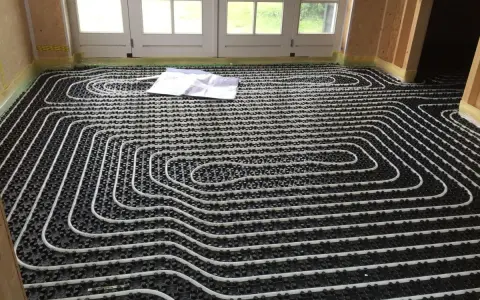 Instalar suelo radiante: tuberías blancas sobre paneles negros, listas para cubrir. Planos en el suelo.