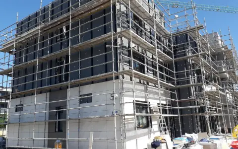 Edificio en construcción con andamios cubriendo la fachada. Se aprecian materiales de aislamiento y paneles, cumpliendo la ley de fachadas.