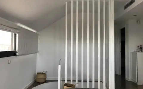 Modern interior with a white slatted divider, suggesting a design to tirar tabique para unir dos habitaciones. Baskets and a window add warmth.
