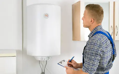 Técnico revisa el funcionamiento termo eléctrico de un calentador de agua, anotando datos en una libreta.