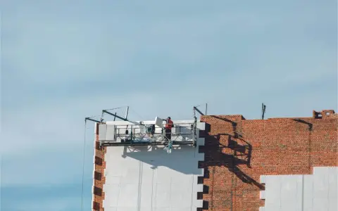 Trabajadores en una plataforma suspendida instalan paneles aislantes en un edificio, parte de un proyecto de sate.