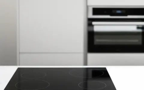 Placa vitrocerámica negra lista para instalar junto a un horno empotrado en una cocina moderna.
