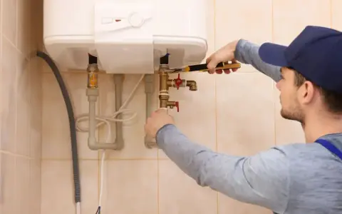 Un técnico ajusta las tuberías de un calentador de agua. Espera que la luz del termo no se apaga para confirmar que todo funciona bien.