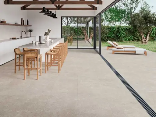 Cocina moderna con isla y taburetes, conectada a terraza con tumbonas. Un proyecto llave en mano que fusiona interior y exterior.