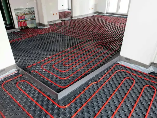 Instalación de un sistema de calefacción por suelo radiante enfria. Tubos rojos serpentean sobre paneles negros en una habitación en construcción.