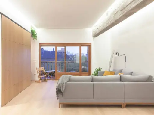 Salón moderno con sofá gris, grandes ventanales y **techos con vigas de hormigón decorar** el espacio con estilo industrial.
