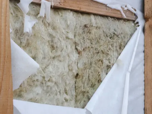 Aislamiento de lana de roca expuesto, con una barrera de vapor blanca rasgada que revela la textura fibrosa.