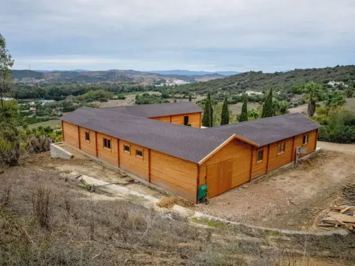 Edificio de madera en forma de L, con tejado oscuro, en un paisaje rural. Ideal para saber cuántos metros cuadrados se pueden construir sin proyecto.