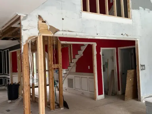 Interior en proceso de demolición, mostrando la estructura de madera expuesta y el cableado. Se observa una escalera roja y paredes parcialmente derribadas, como si se estuviera planeando como tirar una pared de casa.