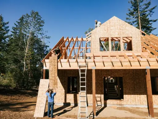Obreros trabajan en la estructura de madera de una casa, mostrando los pasos a seguir para construir una casa.