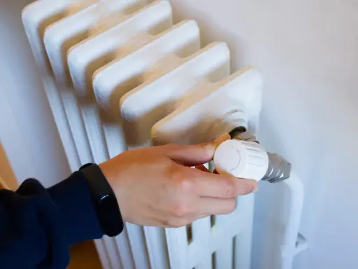 Mano ajustando el termostato de un radiador, parte de los contadores individuales de calefacción central.