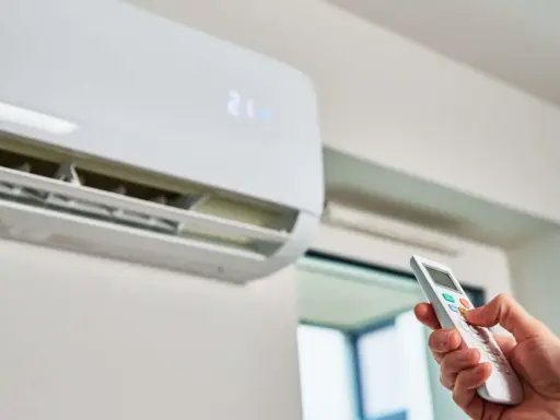 Mano ajustando el control remoto de un aire acondicionado para que gasta menos. La pantalla muestra 21 grados.