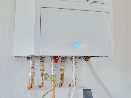 Calentador atmosférico blanco montado en pared con tuberías de cobre y conexiones. Una luz azul parpadea en la unidad, indicando que se puede instalar un calentador atmosférico en el interior.
