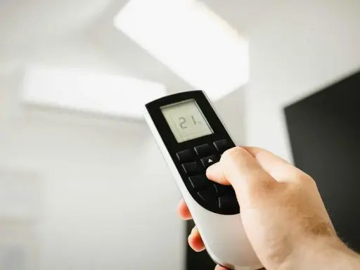 Mano ajustando el mando de aire acondicionado a 21 grados. Instrucciones claras para un confort óptimo.